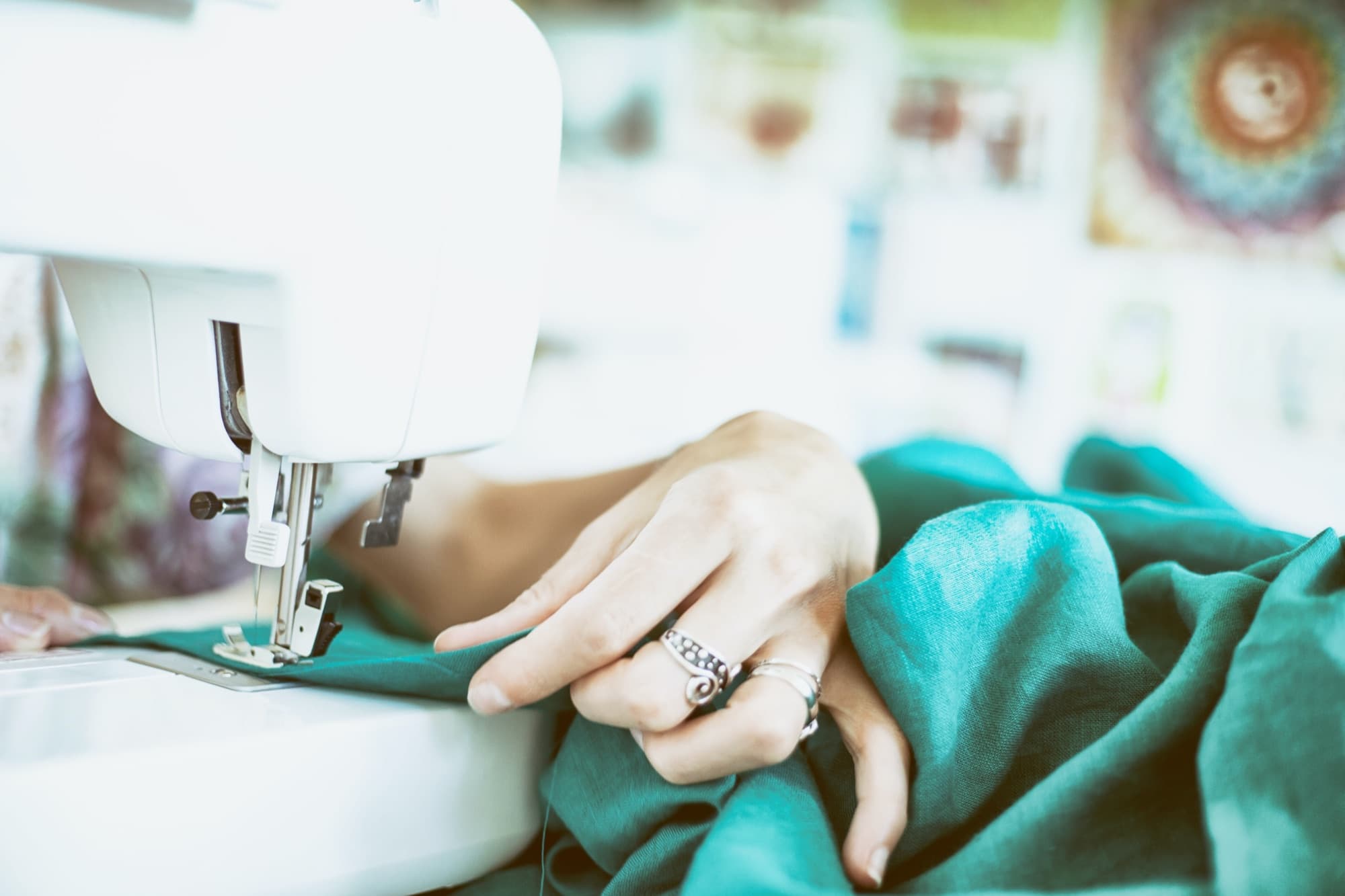 Hands guiding teal fabric through a sewing machine