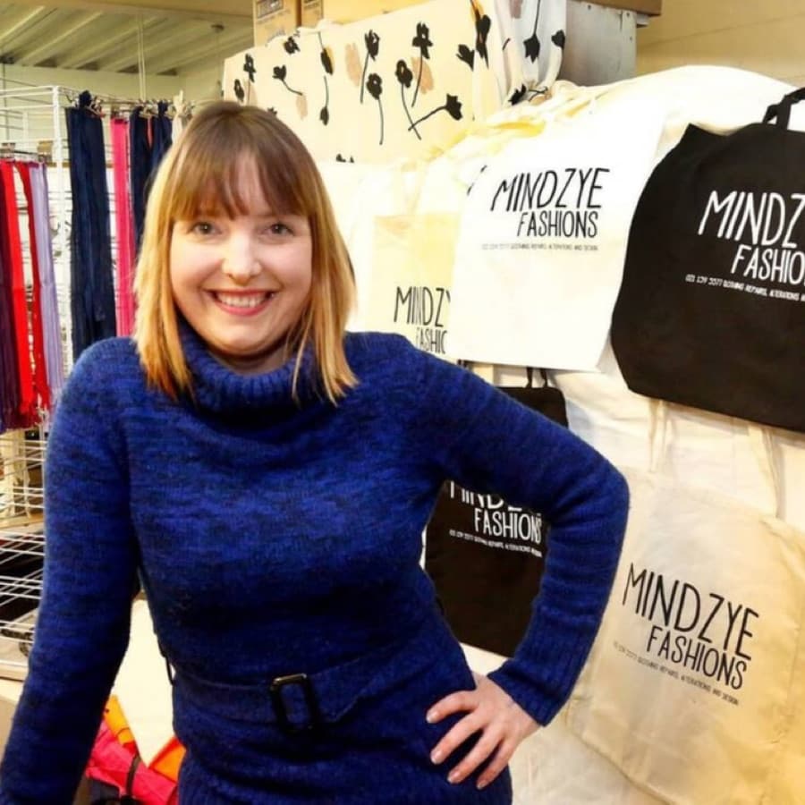 Sara Fredrickson standing in the Mindzye studio beside racks of reusable fabric bags