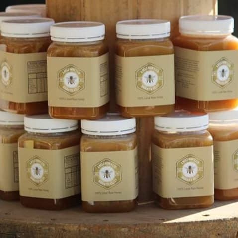 Jars of 4Bees raw Manuka honey stacked on a wooden shelf