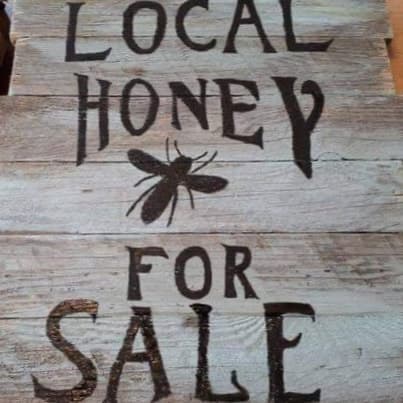 A rustic painted sign reading Local Honey For Sale
